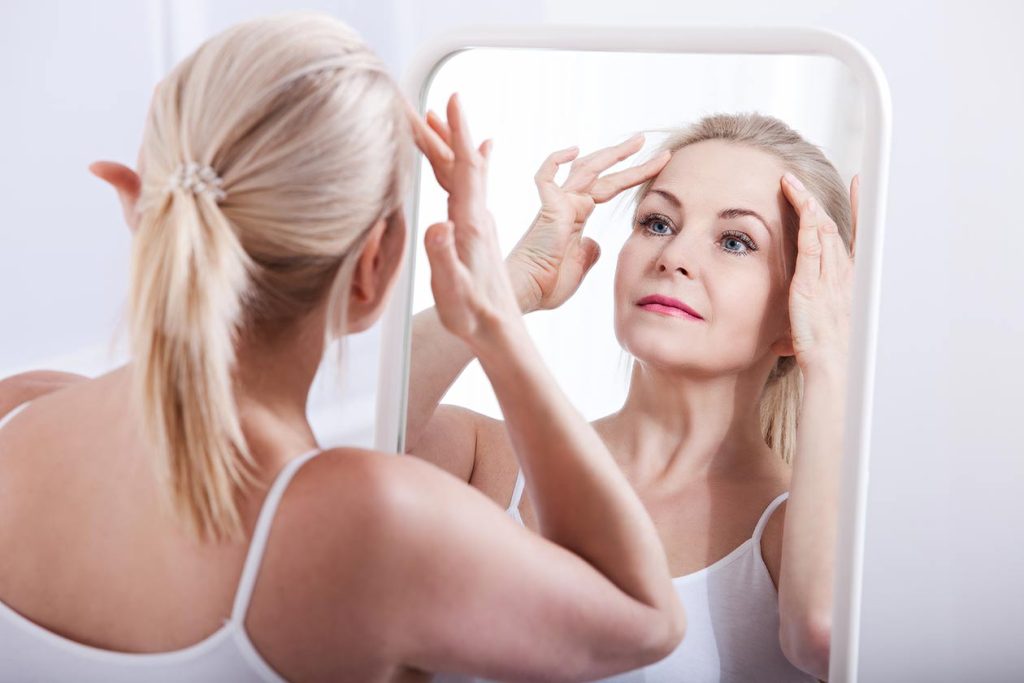 Woman admiring her tight wrinkle free forehead in mirror. Botox Dr. Joshua Korman Wunderbar.
